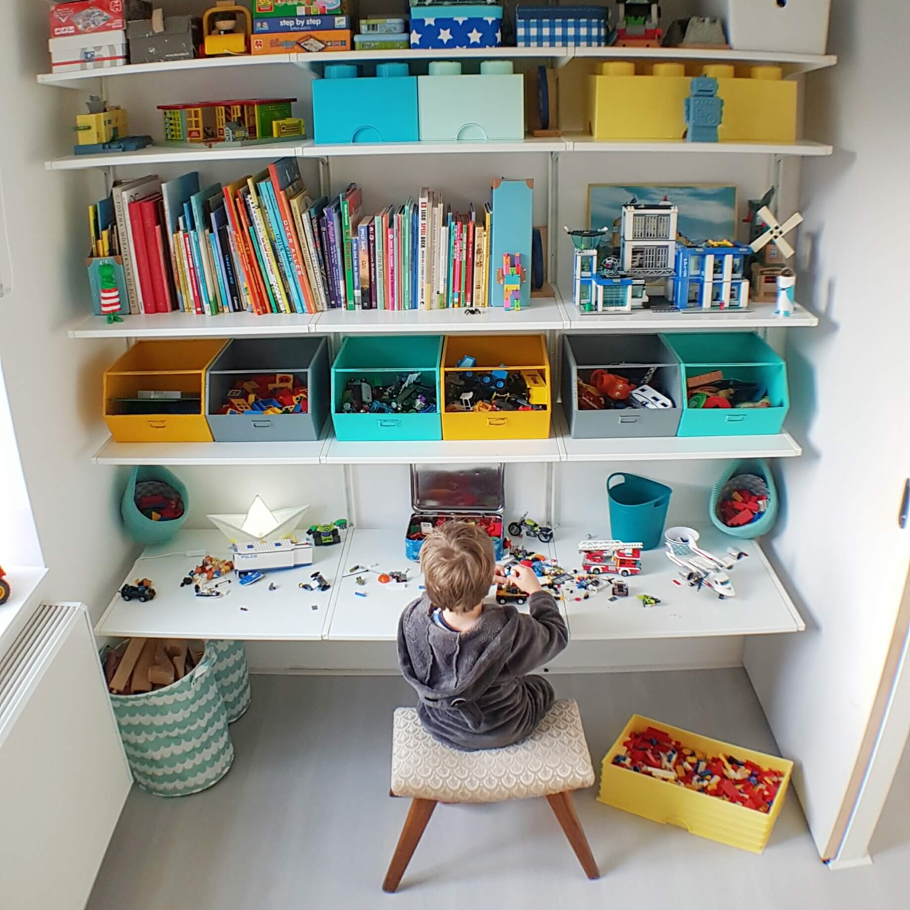 Kleine kinderkamer in geel, turkoois, petrol, kobalt, lichtblauw, mint, groen, grijs en wit. Ikea Algot verstelbare kast, mooi alternatief voor String systeem. Kidsdepot metalen opbergbakken. Lego brick opbergbakken. Goodnight light lampje boot. Yellow blue kids room desk cupboard system.