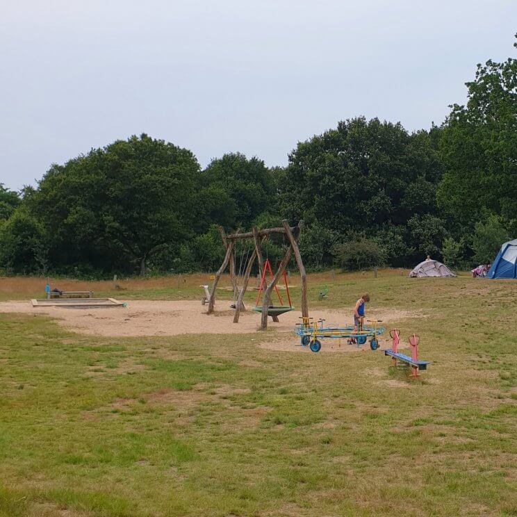 Huttopia de Roos: review van kindvriendelijke natuur camping in Overijssel. Er zijn veel verschillende speeltuinen, dit is de speeltuin naast plek 162. Er is onder meer een gewone schommel, nestschommel, waterpomp, zandbak, wipwap en ronddraaiende fietsjes. 