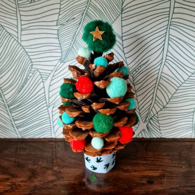 Kerst knutselen: heel veel leuke ideeën. Met een dennenappel en wat versiersels zoals een glimmende pijpenrager en gekleurde bolletjes kun je een kerstboompje maken. 