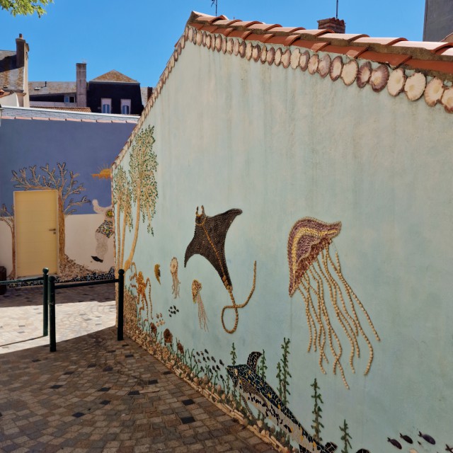 Ben je in de Vendée aan de westkust van Frankrijk? Ga dan zeker naar les Sables d’Olonne. Een leuke stad aan zee, met een heel bijzonder buiten museum. L’Ile Penotte is een schattig klein quartier, met afbeeldingen van schelpen en mozaiek op de gevels. Het is eigenlijk een gratis buiten museum verspreid over een paar steegjes.