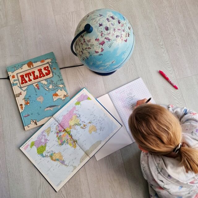 Kleine meis bedenkt haar eigen vakantie project. Ze pakte een stapel atlassen uit de kast en de wereldbol erbij. In haar schrift schrijft ze van alles op over aardrijkskunde.