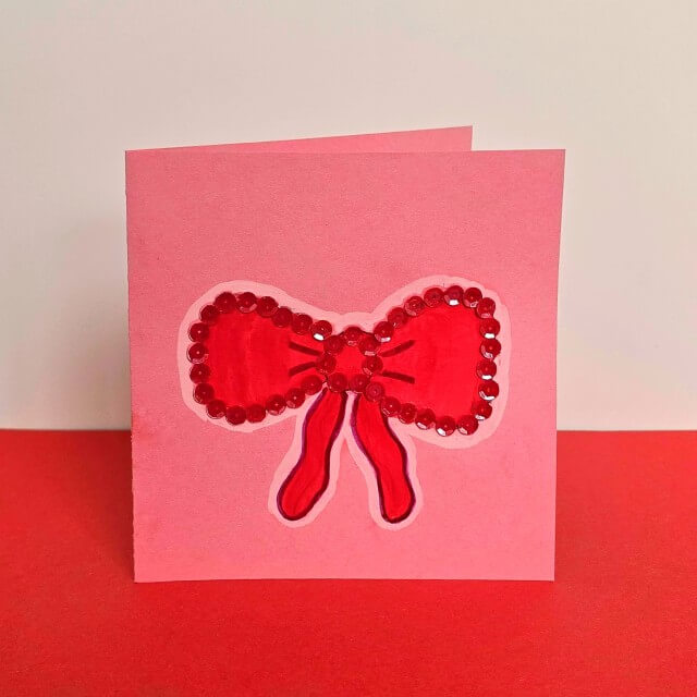 Strik tekenen en knutselen: leuke ideeën voor strikken. Met ideeën voor peuters, kleuters, kinderen, tieners en volwassenen. Deze kaart met strik tekening met pailletten is leuk als kerstkaart.